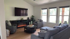 A modern living room with a fireplace, grey sofas, a flat-screen TV, and large windows. - Welcome to your perfect getaway or family retreat in beautiful Magnolia Texas ! (Magnolia)