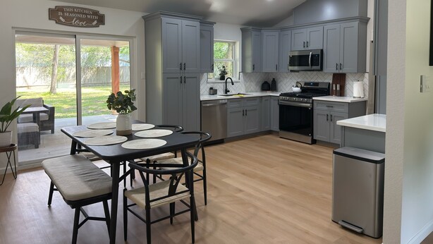 A modern kitchen with grey cabinets, a stainless steel microwave, and a built-in oven. There is a dining area with a table and chairs, and a view of the backyard through large sliding glass doors. - Welcome to your perfect getaway or family retreat in beautiful Magnolia Texas ! (Magnolia)