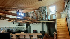 A rustic kitchen with a wooden table and chairs, a stone wall, and a wooden loft. - Characteristic village house, sleeps 10 (Beauvezer)