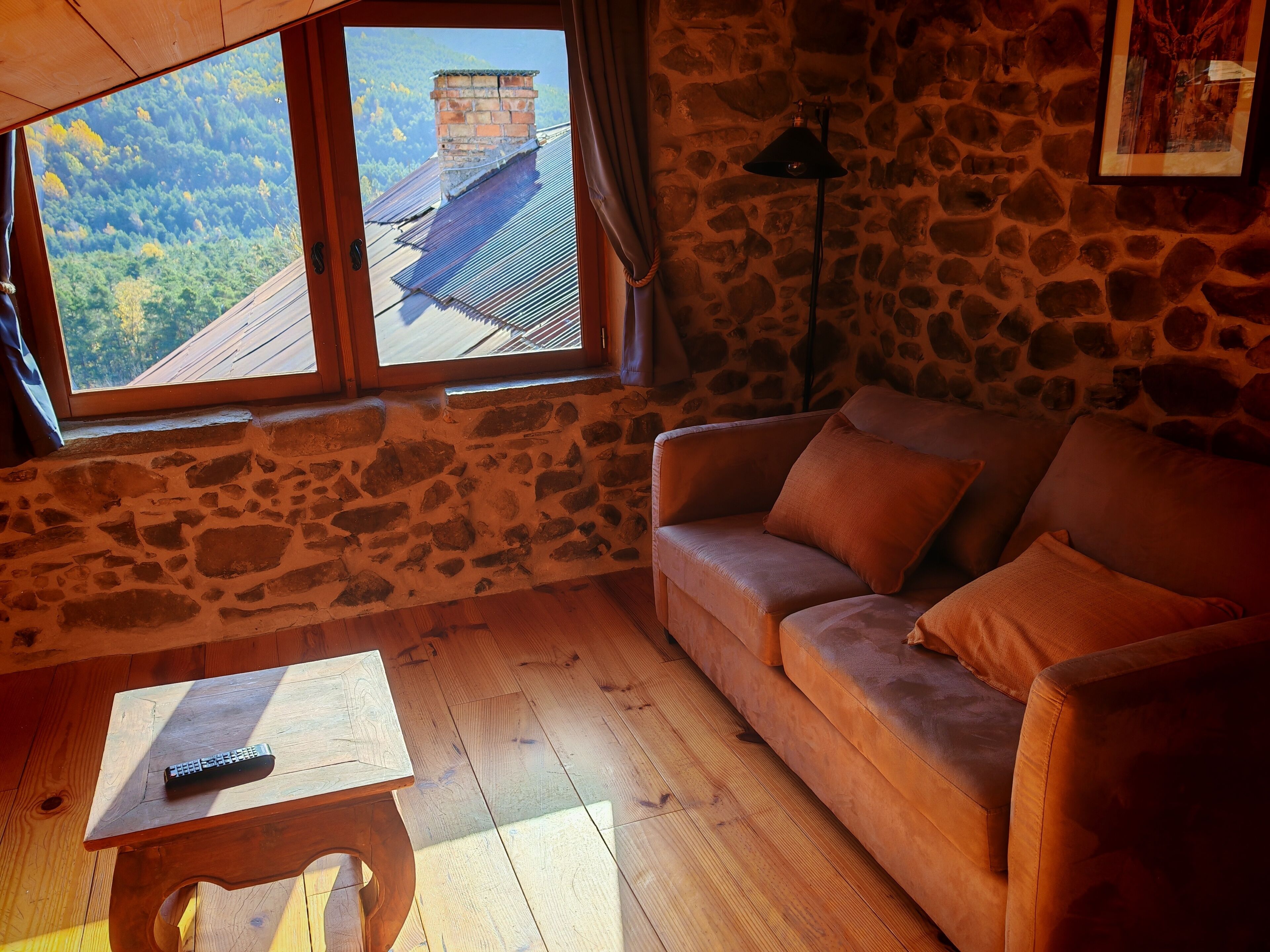 Una habitación acogedora con pared de piedra, suelo de madera, un sofá y una mesa con un control remoto.
