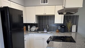 Eine Küche mit weißen Schränken, einem schwarzen Kühlschrank, einer Arbeitsplatte aus Granit und einer gefliesten Spritzschutzwand.
