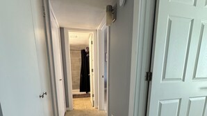 Ein schmaler Korridor mit weißen Türen an beiden Seiten, der zu einem Raum mit Fliesenboden und einer sichtbaren Duschkabine führt.