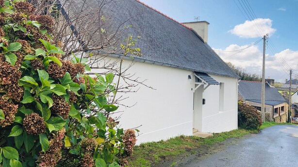 Un bâtiment blanc avec un toit gris, entouré de verdure et sous un ciel dégagé.