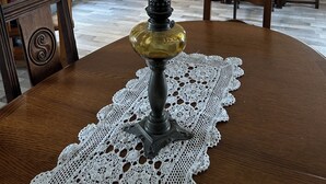 Une table à manger ornée d’un chemin de table en dentelle, une lampe ancienne et une chaise en bois.