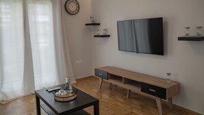A modern living room with a wooden floor, a black TV on the wall, a wooden bench, and a small table with a glass pitcher and glasses. - Seaside Charm in Palaio Faliro – Walk to Beach & Cafés! (Paleo Faliro)