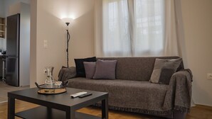 A living room with a sofa, a coffee table, a lamp, and a kitchen area in the background. - Seaside Charm in Palaio Faliro – Walk to Beach & Cafés! (Paleo Faliro)
