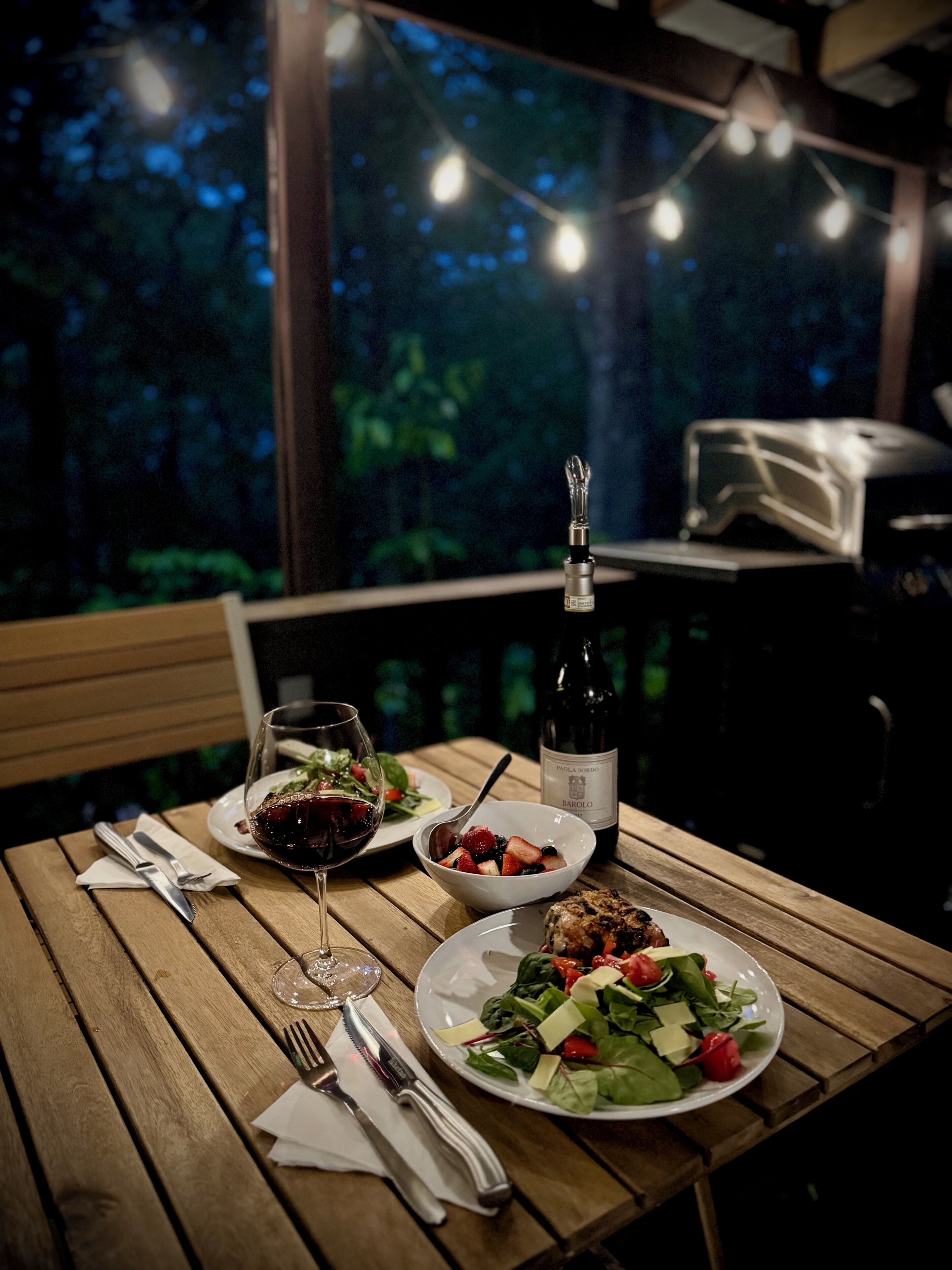 A wooden dining table with plates of food, a wine bottle, and glasses.
