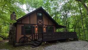 A cabin with a stone chimney, a wooden porch, and a wheelbarrow. - Angler's Chalet (Topton)
