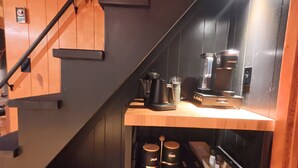 A staircase with wooden steps and a metal handrail, leading to a room with a wooden table, a coffee maker, and two containers labeled "sugar" and "cream". - Angler's Chalet (Topton)
