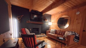 A cozy living room with a fireplace, wooden furniture, and a round mirror on the wall. - Angler's Chalet (Topton)
