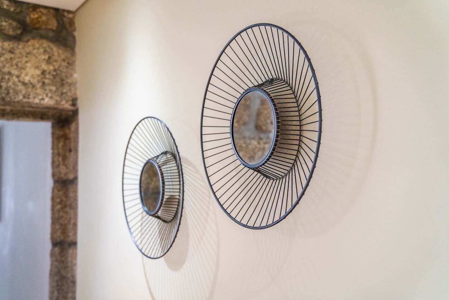 Two wall-mounted circular mirrors with a wireframe design against a plain wall.