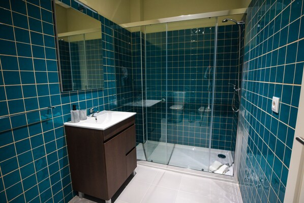 Une salle de bain avec des carreaux de couleur turquoise, une douche en verre et un lavabo blanc.