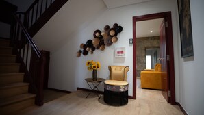 Un escalier, une table ronde ornée d’un vase de tournesols, un fauteuil à capitons et un canapé jaune dans une pièce bien éclairée, dotée d’un plancher en bois.
