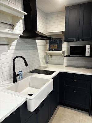 Una cocina moderna con muebles blancos y oscuros, una campana extractora negra, un horno integrado, un microondas y un lavabo con grifo.