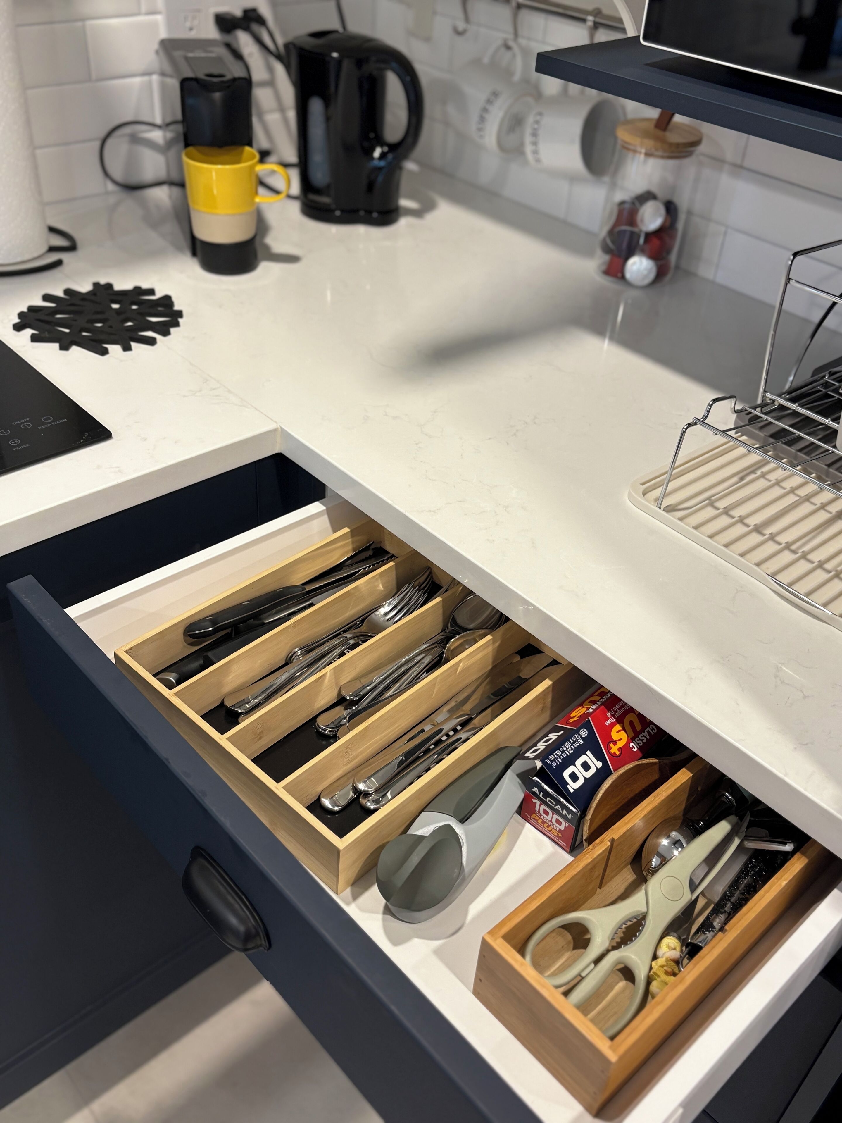 A kitchen with a drawer containing utensils, a coffee maker, and a jar of spices.