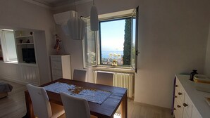 A dining area with a table set for two, a television, and a view of the sea through a large window.