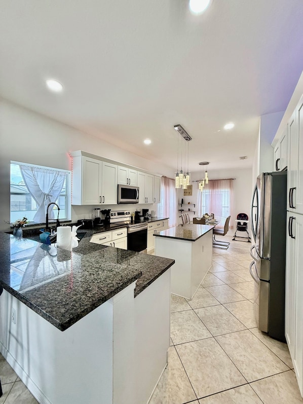 A modern kitchen with white cabinets, granite countertops, a central island, stainless steel appliances, and pendant lighting.