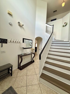 A staircase with a handrail, a wall-mounted mirror, a console table with a lamp, and a bench. - 5BR HOME W/PRIVATE POOL& GAME ROOM CLOSE TO MAJOR ATTRACTIONS (Kissimmee)