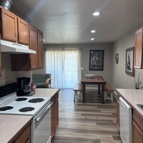 Una cocina con armarios de madera, una estufa, una cafetera y un comedor con mesa y sillas.