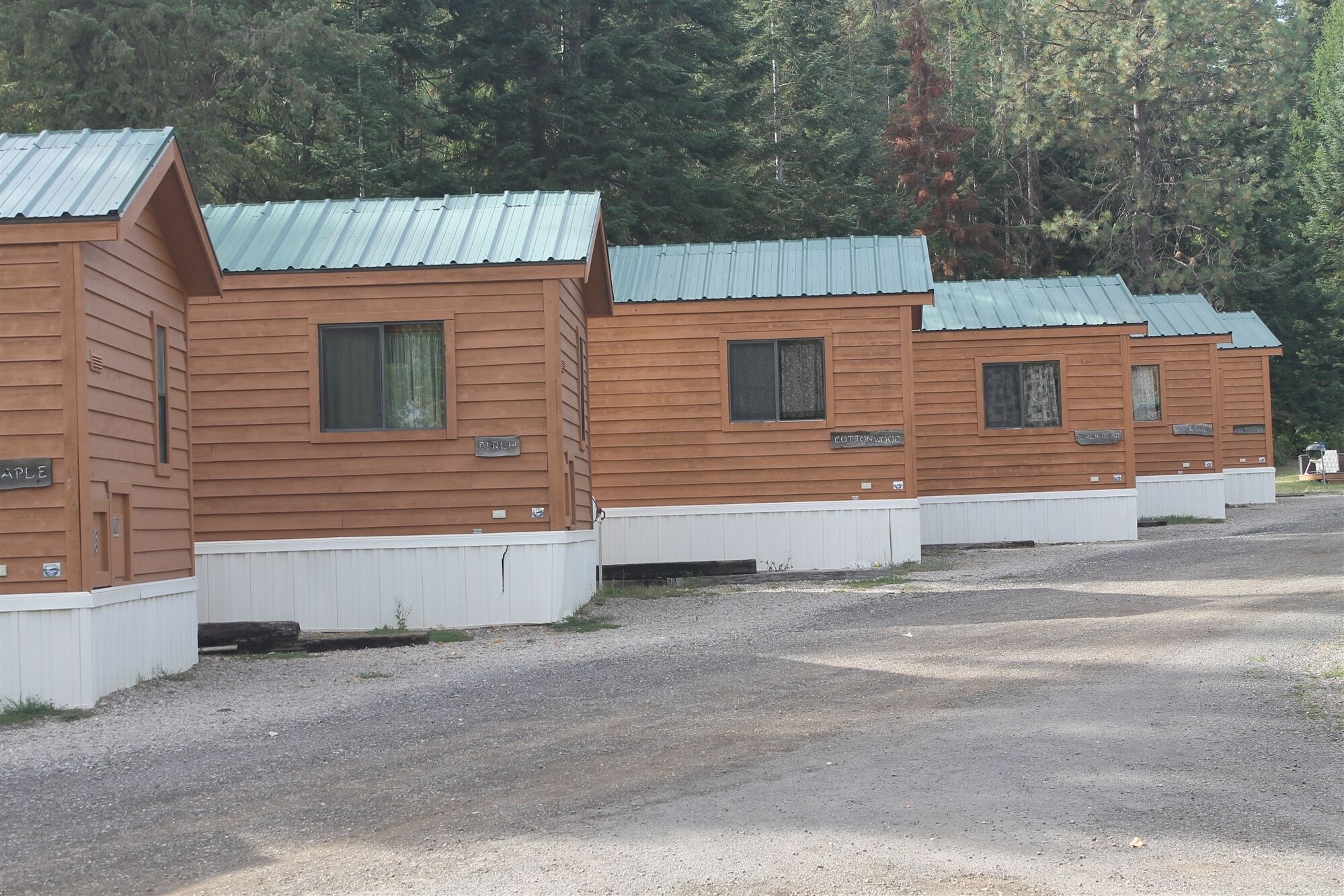 Une rangée de cabanes en bois, coiffées de toits en métal, chacune dotée d’une petite fenêtre et d’une plaque nominative.