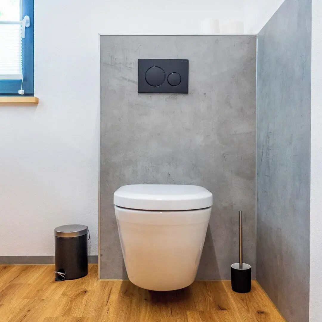 A modern bathroom with a white toilet, a wall-mounted bidet, a trash bin, and a floor lamp.