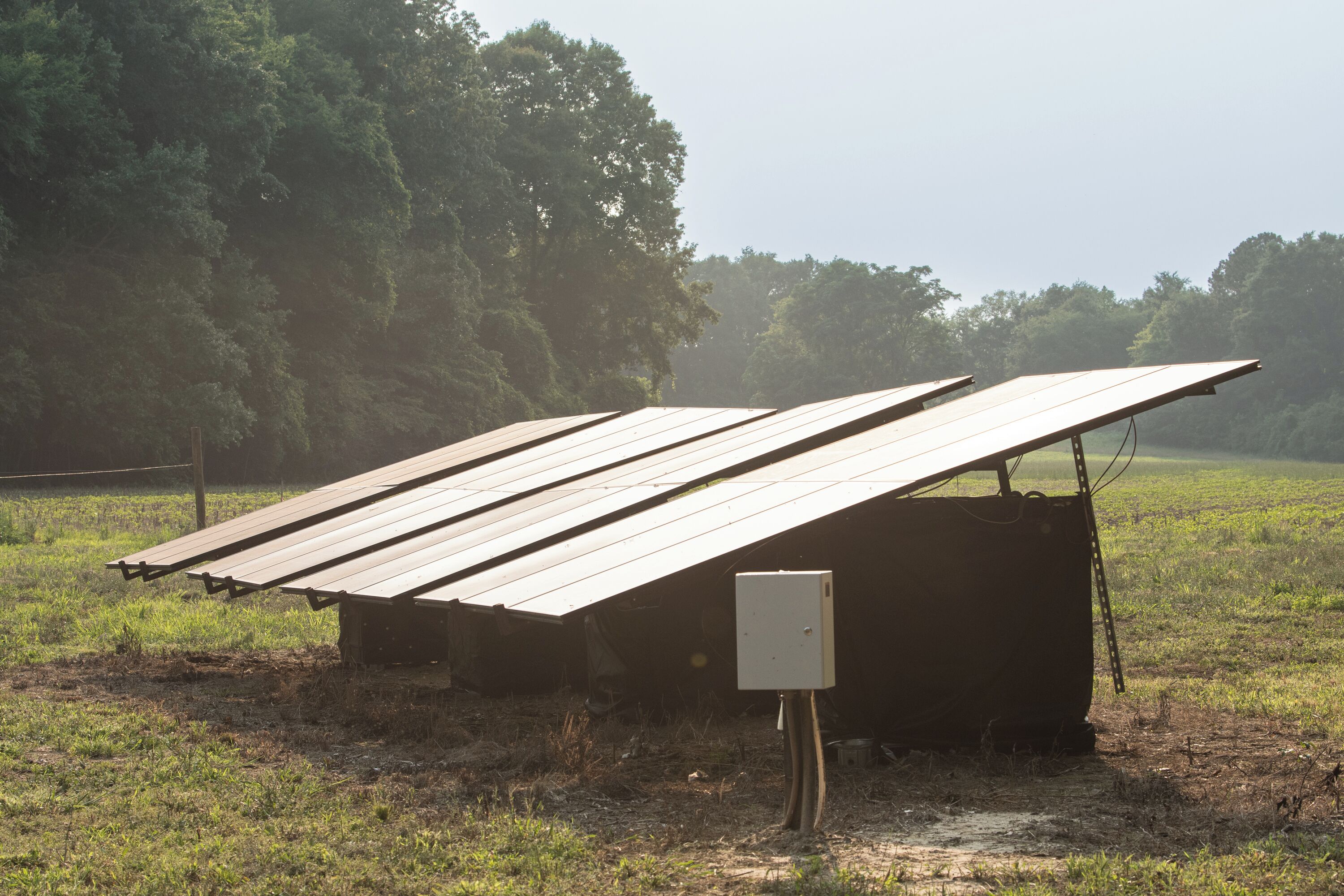 A solar panel installation with a metal box and wooden beams in a grassy field.