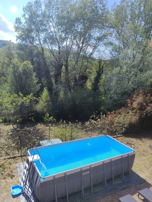 An outdoor swimming pool with a safety ladder, surrounded by trees and vegetation.