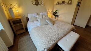 A bedroom with a bed, bedside tables, a bedside lamp, a wall-mounted shelf with pictures, and a wooden floor. - Cottage Wisterya in Piemonte with pool (Piemonte)