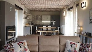 A living room with a sofa, two cushions, a dining area with a table and chairs, and a kitchen in the background. - Villa Pietra with pool on the Piemonte Hills (Piemonte)