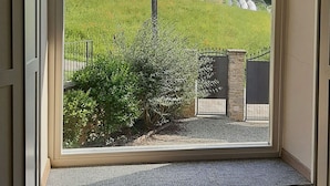 A room with a large arched window offering a view of a green field, a stone wall, and a distant building. - Villa Pietra with pool on the Piemonte Hills (Piemonte)