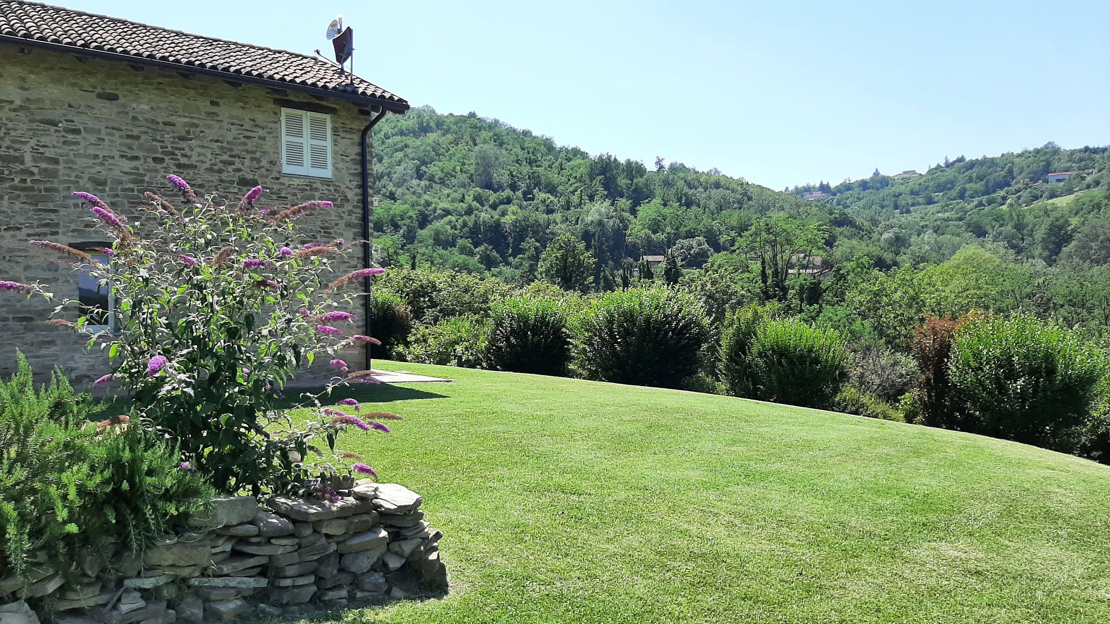 A stone building with a tiled roof, a stone wall, and a well-maintained grassy lawn.