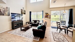 Un salón espacioso con un televisor de pantalla plana grande, sofá de cuero y una zona de comedor con mesa de cristal.