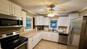A kitchen with white cabinets, a stainless steel refrigerator, a microwave, an oven, and a ceiling fan.