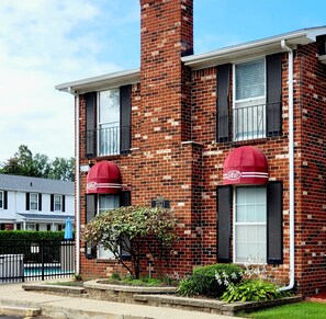 A two-story brick building with a red awning, a visible address sign, and a small garden area with plants.