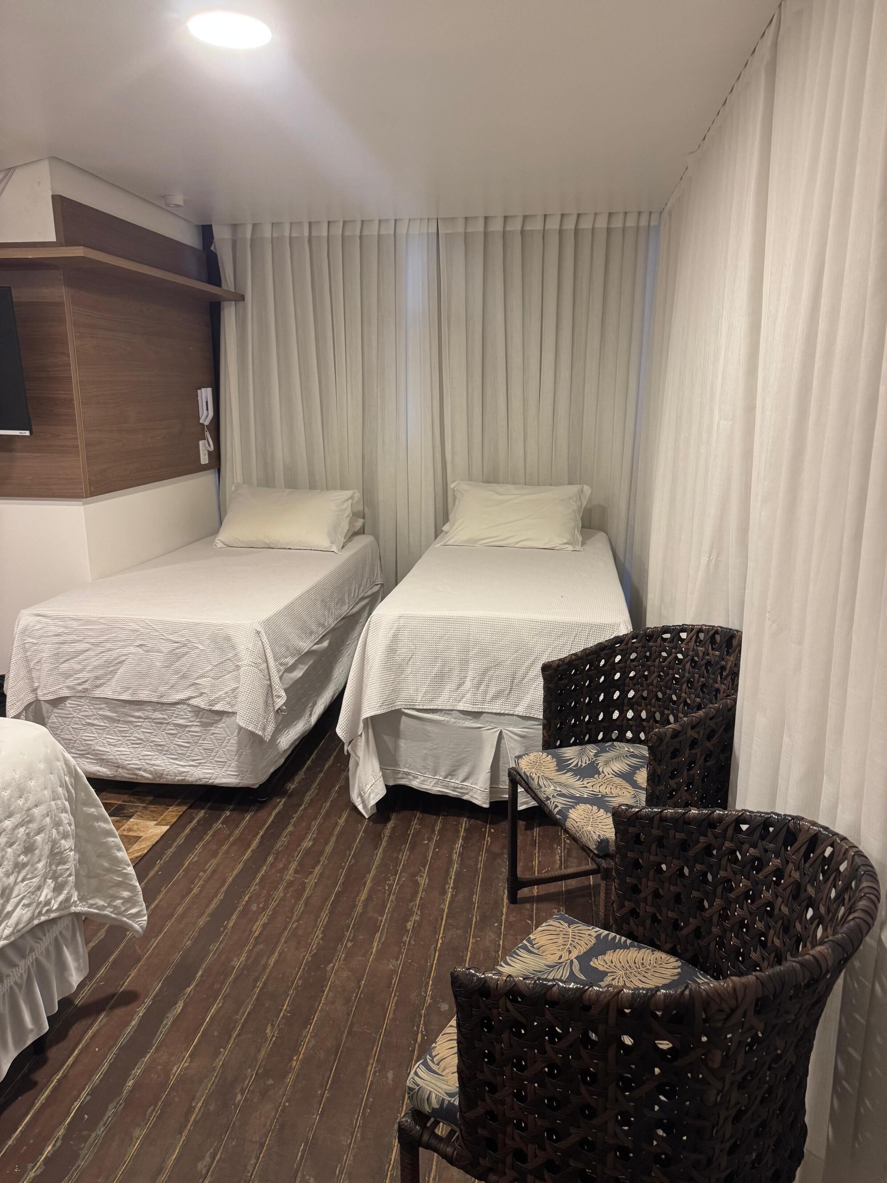 Habitación de hotel con dos camas, una silla de mimbre y suelo de madera.