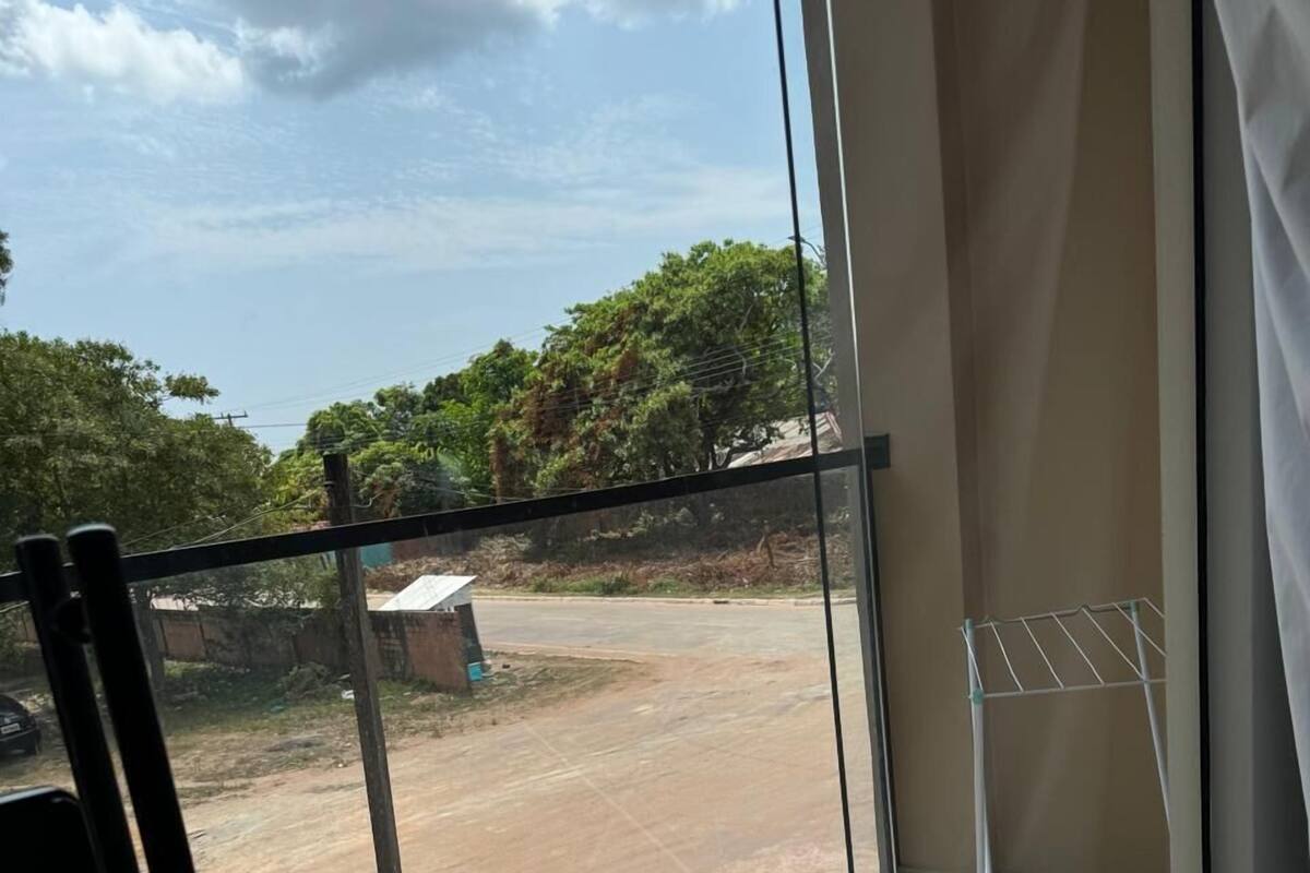 Ein Balkon mit Glastür, einem Wäscheständer aus Metall und Blick auf eine unbefestigte Straße und Grünflächen.