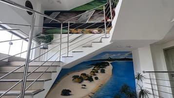 Interior com vários níveis, incluindo uma escadaria, um mural com uma cena de praia e plantas em vasos.