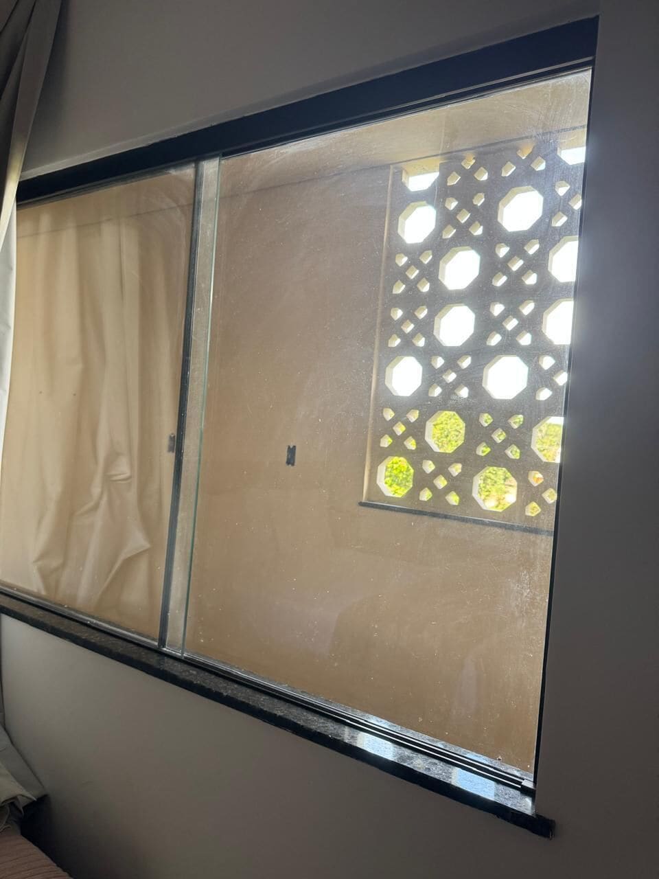A window with a view of a building's exterior, a curtain, and a decorative window screen.