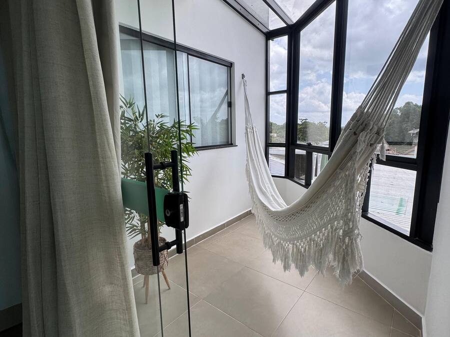 Una habitación con hamaca, una silla, una planta en maceta y vistas amplias a través de grandes ventanales.