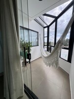 Una habitación con hamaca, una silla, una planta en maceta y vistas amplias a través de grandes ventanales.
