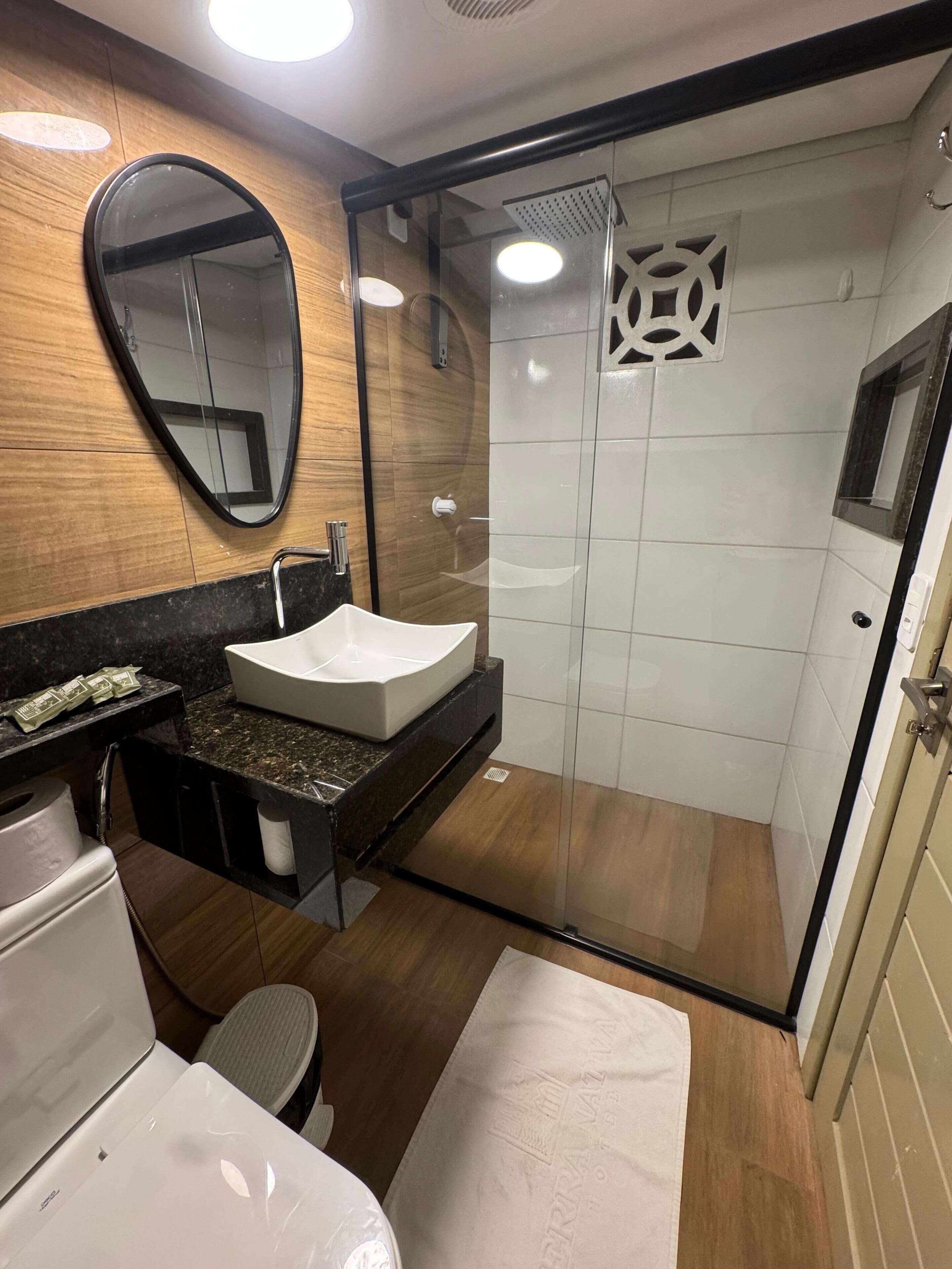 A modern bathroom with a white sink, a mirror, a shower, and a toilet.