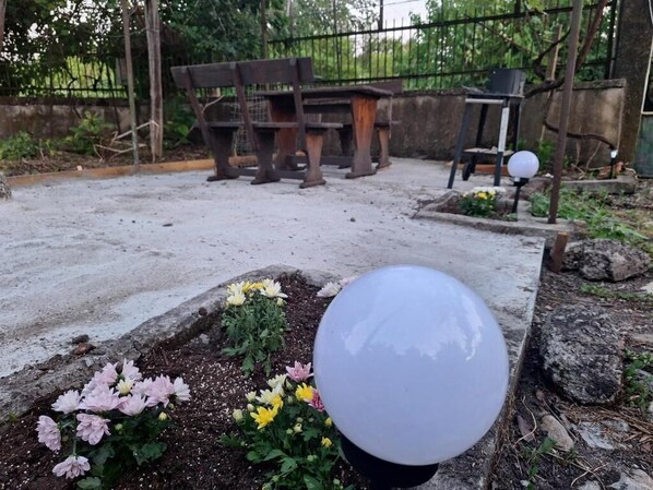 A garden area with a concrete path, a flower bed with pink and yellow flowers, and a wooden bench in the background.