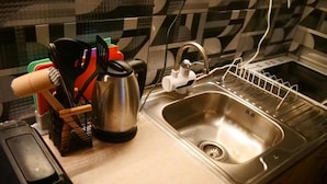 A kitchen with a stainless steel sink, a kettle, and various utensils.