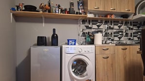 A compact kitchen with a washing machine, a refrigerator, wooden cabinets, and a patterned backsplash.