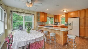 A kitchen with wooden cabinets, a central island with stools, a ceiling fan, and a large window with a view of greenery. - Fish, Hike & Unwind: Remote Home in Ararat! (Ararat)