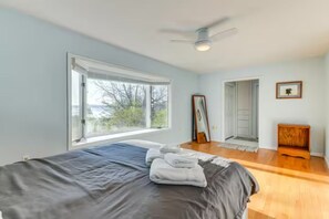 Une chambre à coucher comprenant un lit, un ventilateur de plafond, une fenêtre et une porte donnant sur une autre pièce.