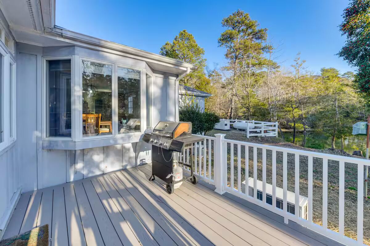 Eine überdachte Terrasse mit Grill, weißen Geländern und Blick auf einen See und Bäume.