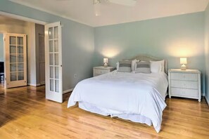 A bedroom with a large bed, two bedside tables with lamps, and a door leading to another room.