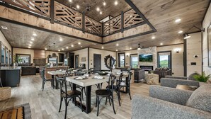 A spacious open-plan living area with a dining table, multiple seating arrangements, and a fireplace. - Brand New Ultra Lux 8BR Cabin with Indoor Pool, Theater, Waterpark Access, & PS5 (Sevierville)
