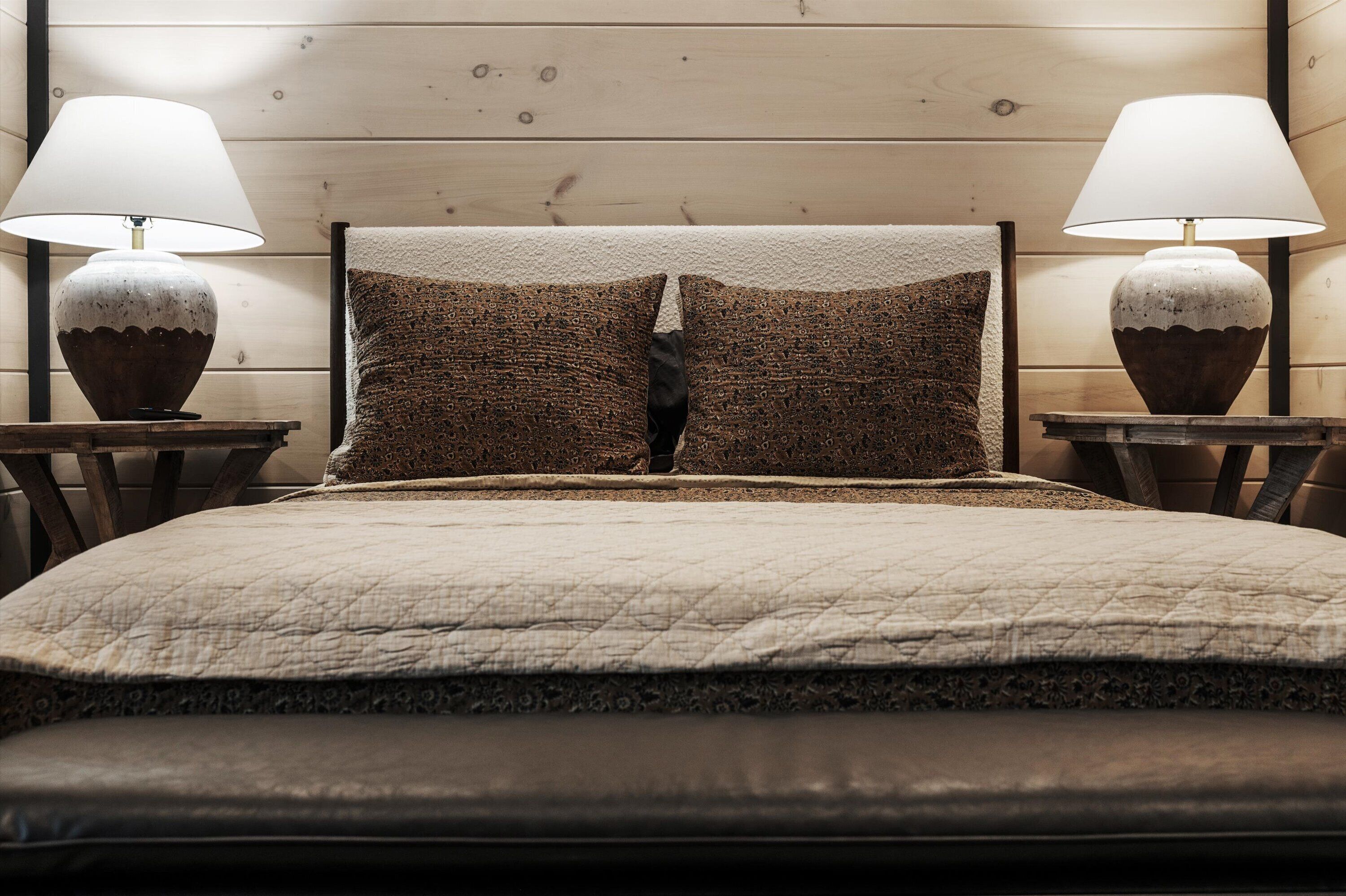 A bedroom with a wooden headboard, two bedside lamps, and a quilted bedspread.